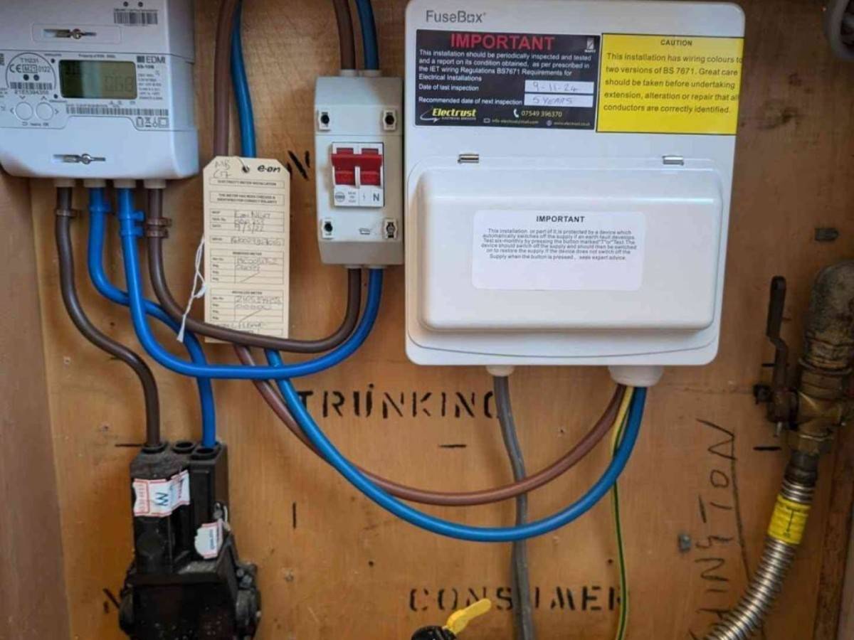 An electrical setup featuring a FuseBox branded unit, wiring, and meters installed on a wooden panel. The image includes an Electrust Electrical inspection label and neatly arranged blue and brown wires.