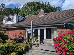 A professional electrician working on a residential property with tools and equipment, ensuring safe electrical installations. Lush garden and patio area in view. Electrust Electrical, 24-hour emergency electrician services.